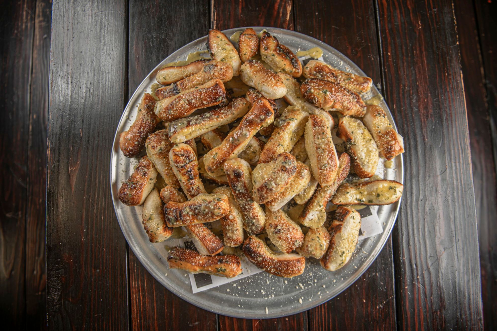 A tray piled with garlic breadsticks dusted in parmesan